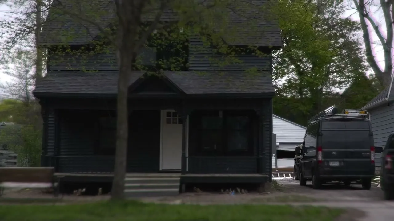 The restored Victorian from across the street, dark siding and black trim under spring trees