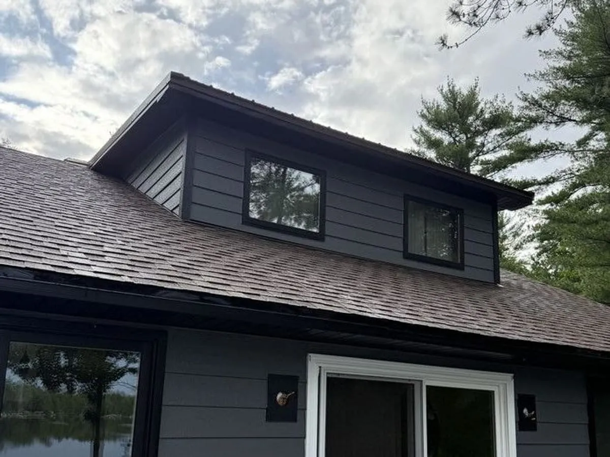 The lakeside house from the deck: dark lap siding, black-trimmed dormer and a slider to the water